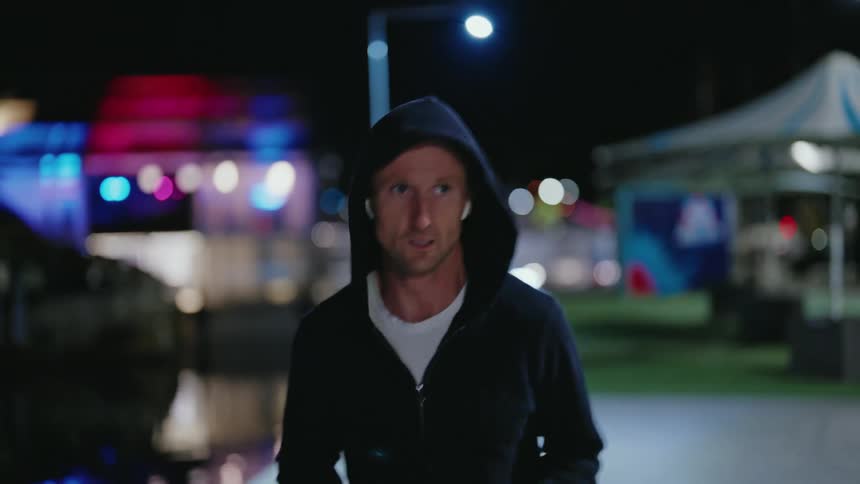 Man with dark blue hoodie with zipper white shirt and smartwatch jogs along promenade at night