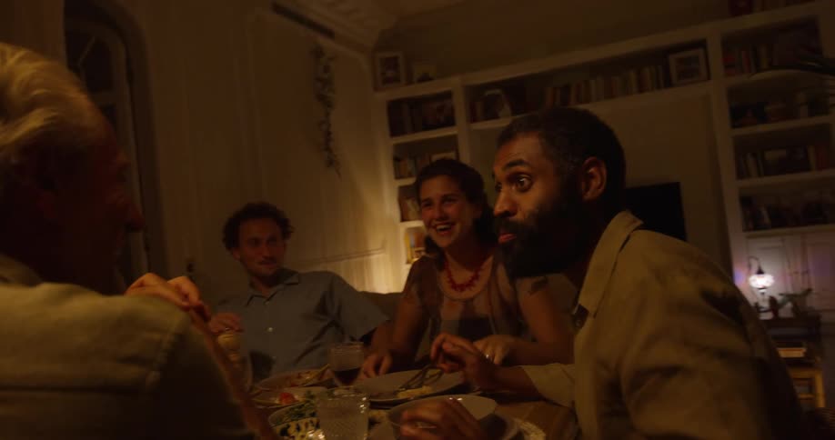 People sitting at table dine by candlelightand talk with each other in room