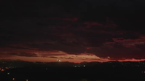 Airplane flies toward a landing at night through a red sky over city lights