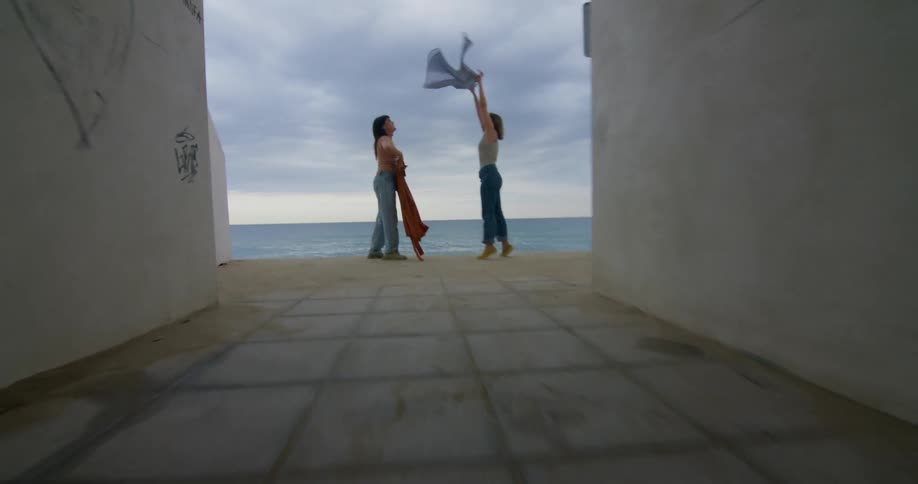 Women hold tops over their heads as they stand at end of tunnel overlooking beach