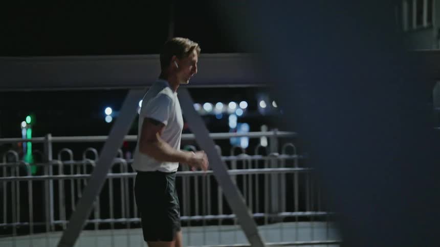 A man checks his watch while jogging in place then begins to run across the bridge