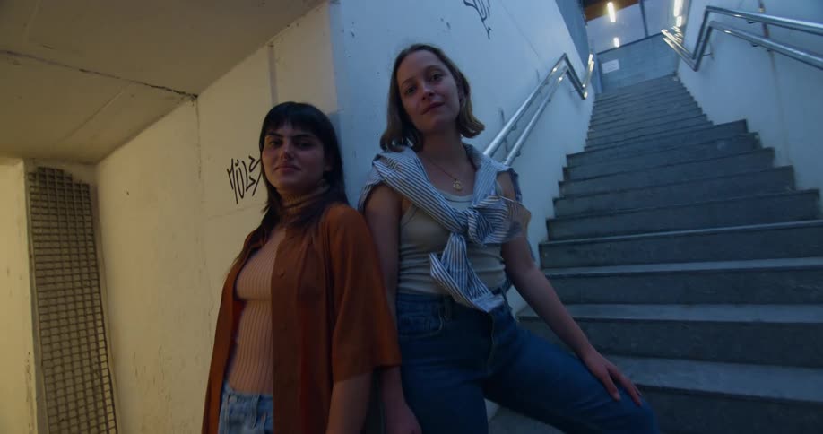 Two women pose together at base of staircase near graffiti dotted walls