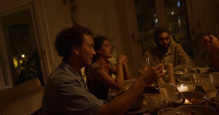 Friends sit at table at night during dinner party and talk