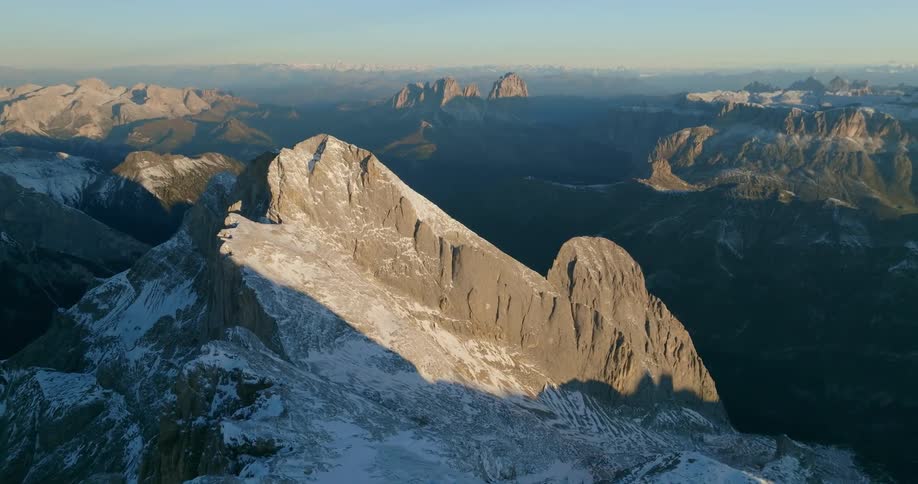 Snow covered mountain slope sits partially in shadow overlooking valley and misty horizon