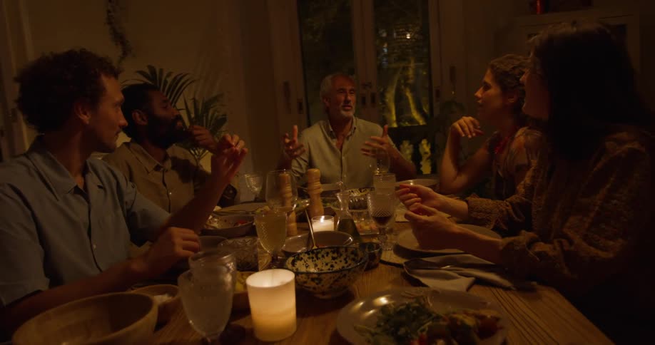 A group of people sit at a dining table in a home and talk