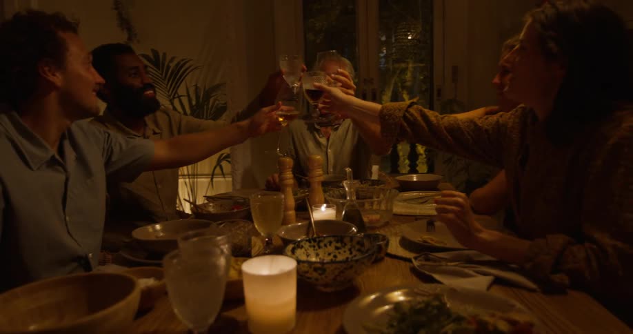 Friends sitting around dinner table at night share a toast