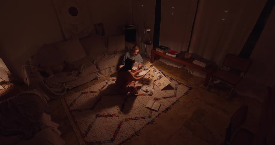 Two teenage girls work on a school project in a living room