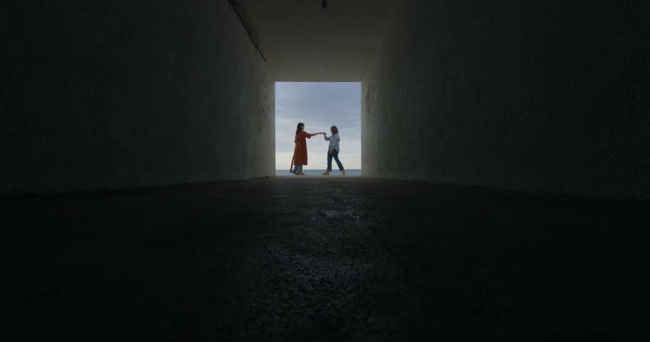Two women at opening of long tunnel dance against sky and ocean