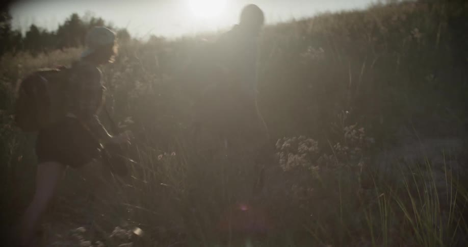 Two people hike up a grassy hill