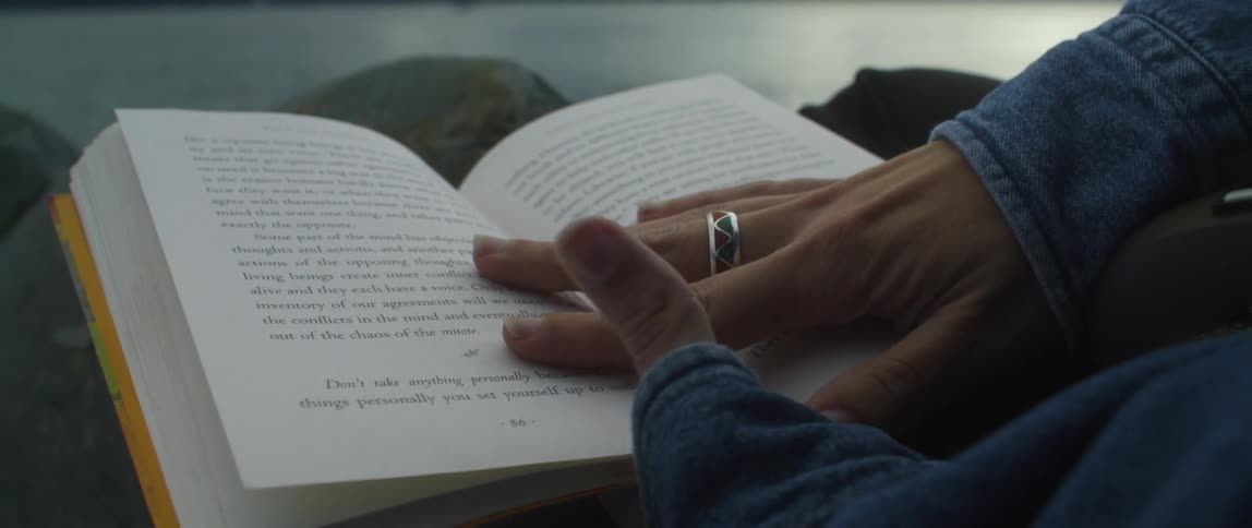 A woman is looking at a book and resting her hand across the pages as she turns them