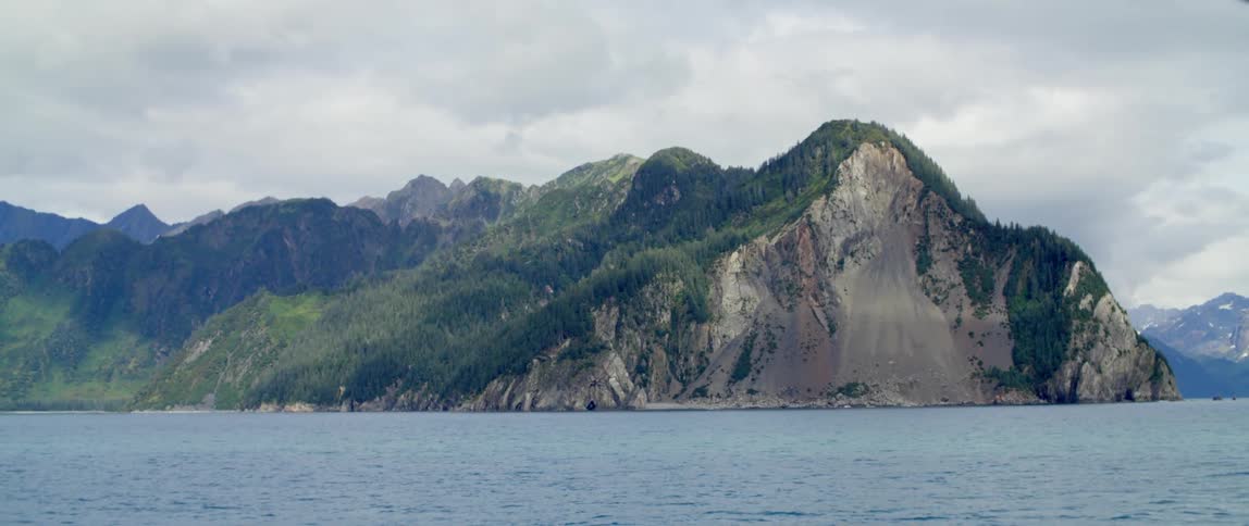 A mountain ridge covered in vegetation on the coast on a cloudy day