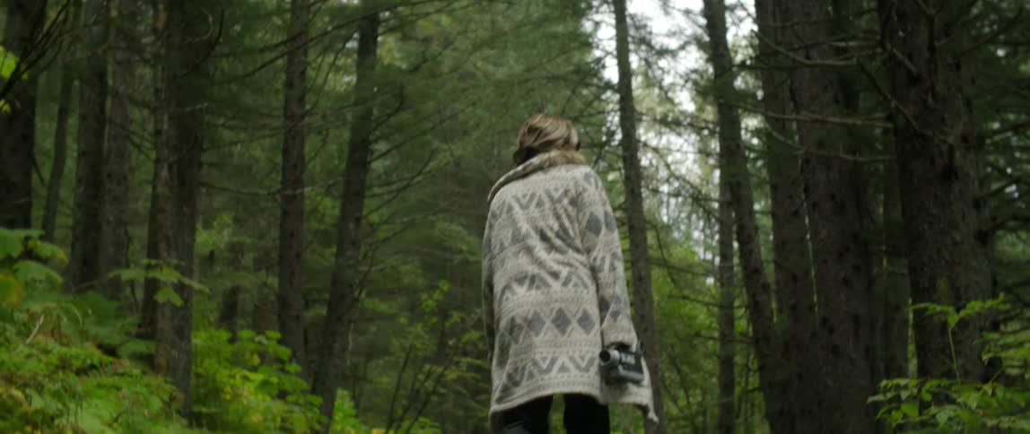 A woman wearing a long sweater is walking on a trail through the woods