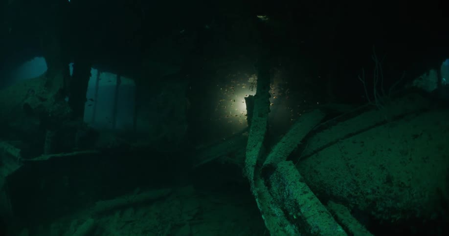 Scuba divers carrying bright lights explore ship wreck