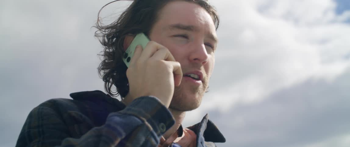 A man talks on a smartphone while standing outdoors during the day