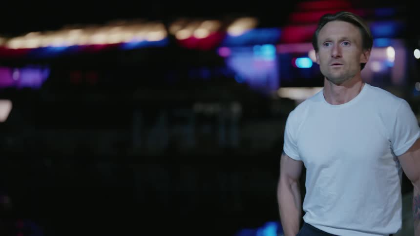 A man stretches his legs and places earbuds in his ears before beginning to jog along a waterfront at night