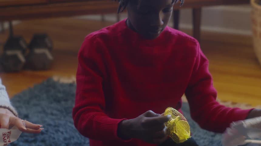 Kid pulls foil wrapped chocolate coins from giftwrapping while sitting on floor rug