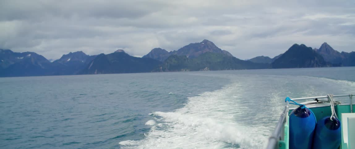 A speedboat travels away from a mountain range