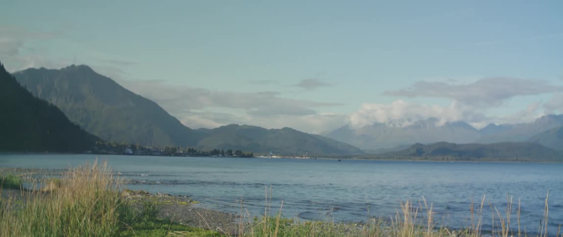 Fog blows over beachacross water from boats moored near town sitting at base of mountains