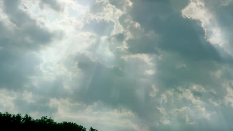 Sun rays shine down between moving clouds