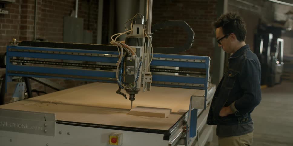 A man watches a machine cut wood