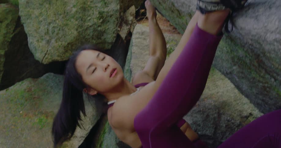 A woman reaches up a rock face then lifts her leg to a foothold as she climbs