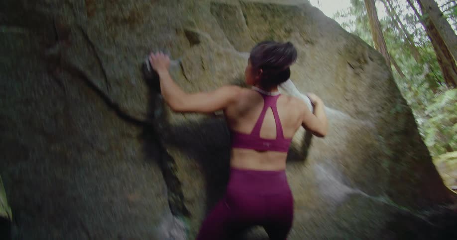 A woman climbs a natural rock face in a forest during the day