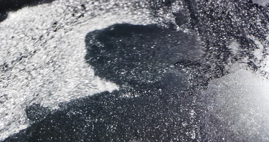 Water breaks through gray ice sheet pulling pieces off