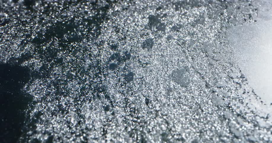 Flowing melt water sparkles as it pulls sections from ice sheet