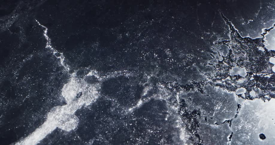 Water running and bubbling over the layer of frozen ice on the surface of a body of water