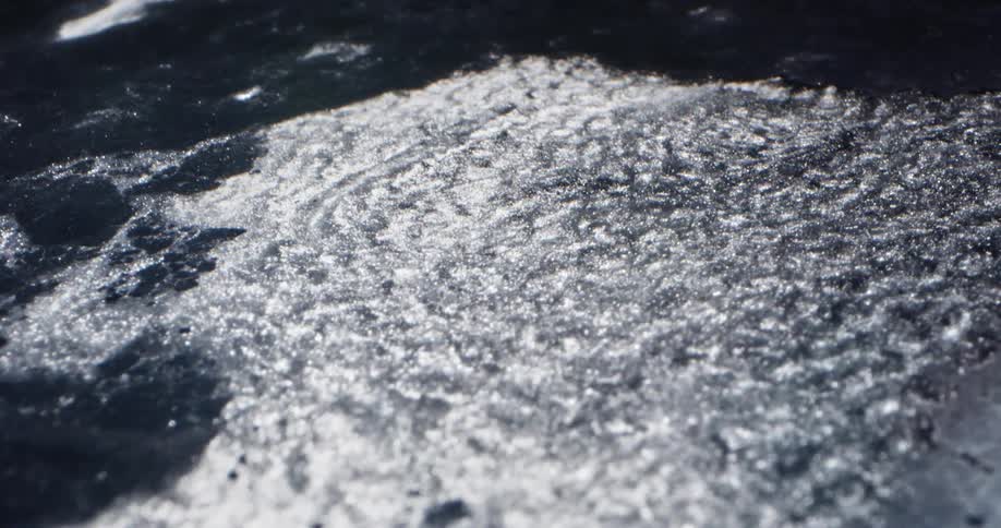Shimmering water flowing breaking up surface ice