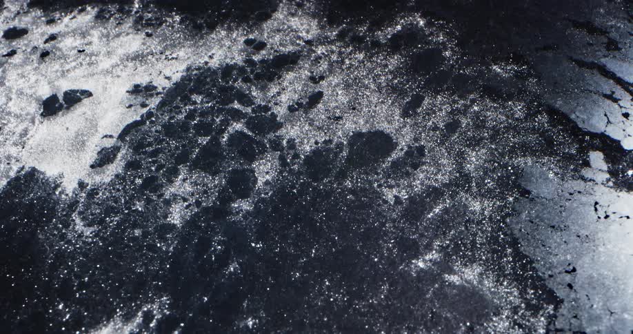 Thawing water sparkles white while breaking through gray ice sheet