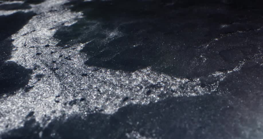 Water flows down slope widening gap in gray tinted sheet of ice