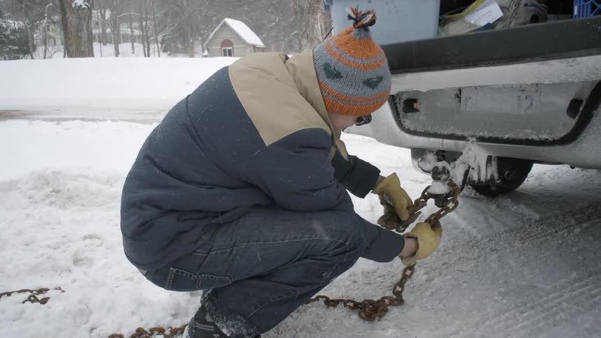 A man wraps a chain around a hitch on a vehicle