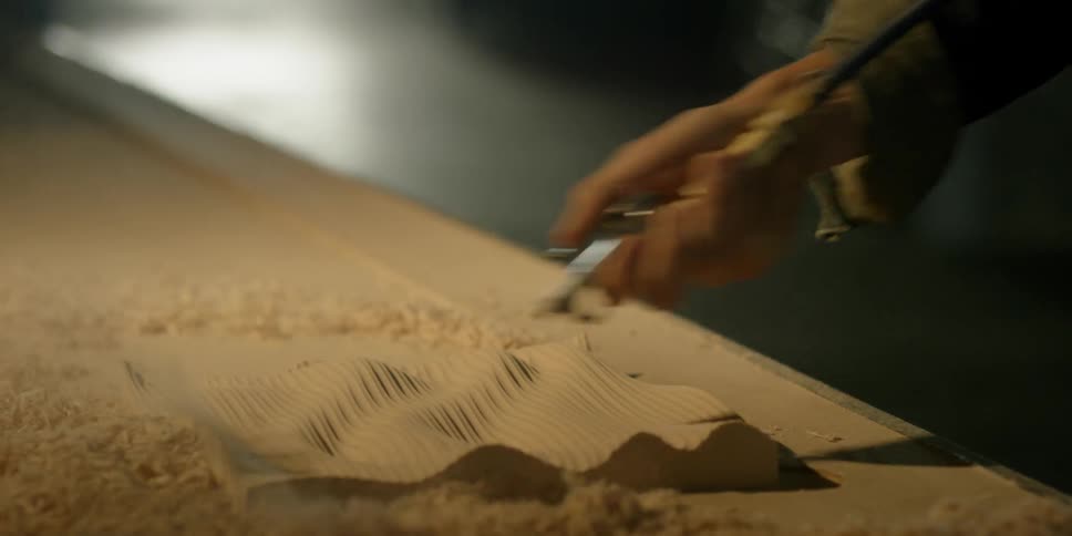 A person blows wood chips off a piece of wood