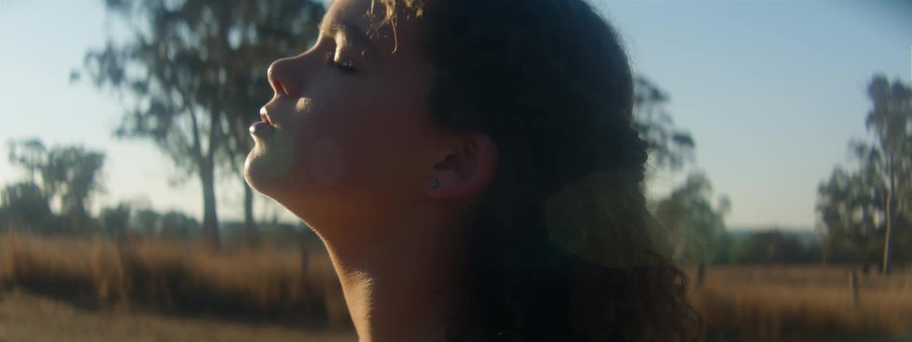 Side profile of woman with curly hair looking up in the field eyes closed