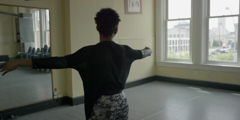 A woman goes through dance moves in front of a mirror in a studio