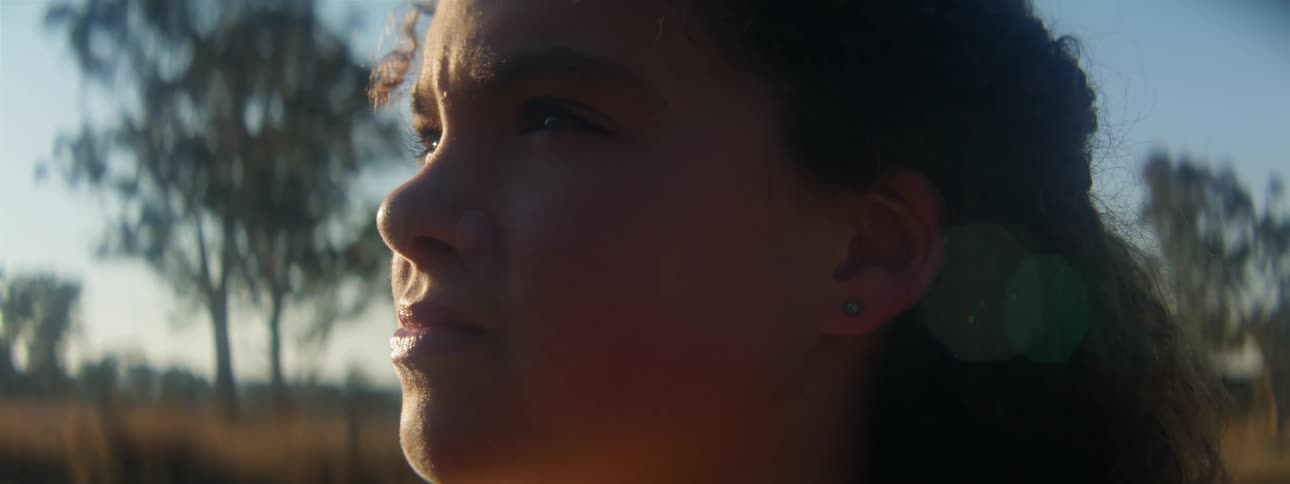 A young woman is standing outdoors in a rural area contemplating during the evening