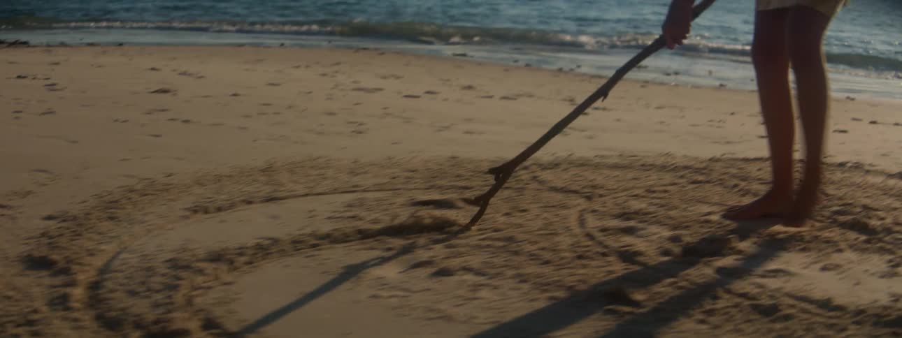A female draws in the sand with a long stick