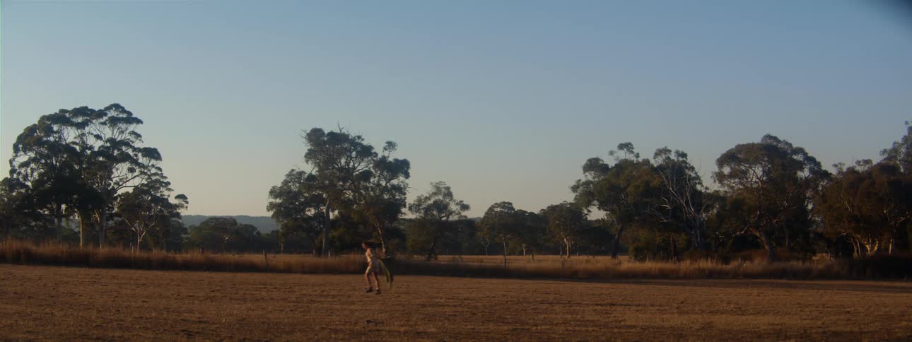 Woman runs and skips across pasture under clear sky