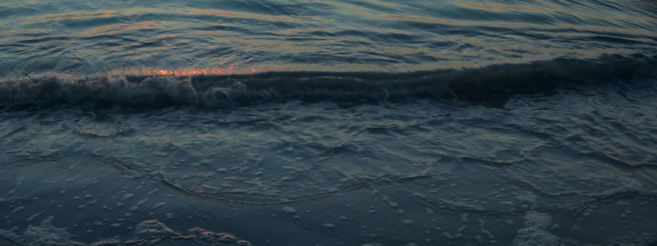 Small waves landing on a beach at dusk with the setting sun reflecting on the waves