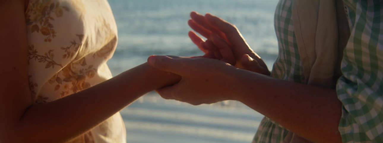 A woman putting a gift into another womans hand on a beach