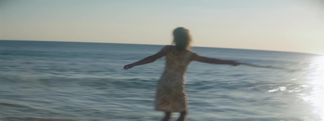 A woman on the beach spins around in circles while holding a branch
