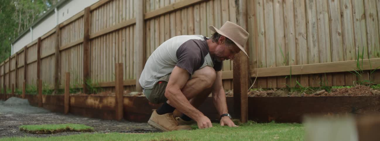 A man lays sod in a yard