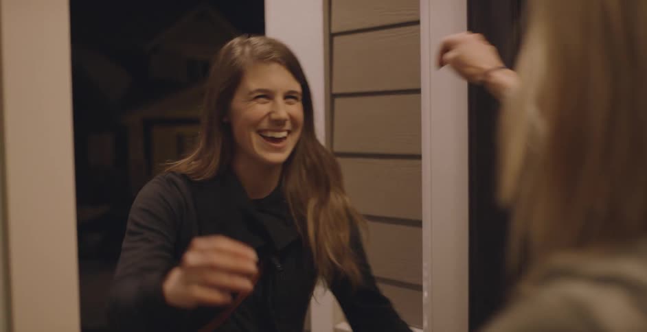Blonde woman at the door welcomes woman with brown hair and black zip up hoodie