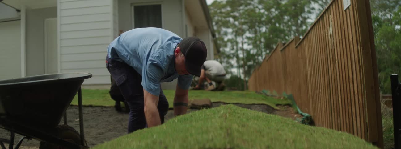 Three men are outside laying down sod in a yard around a house