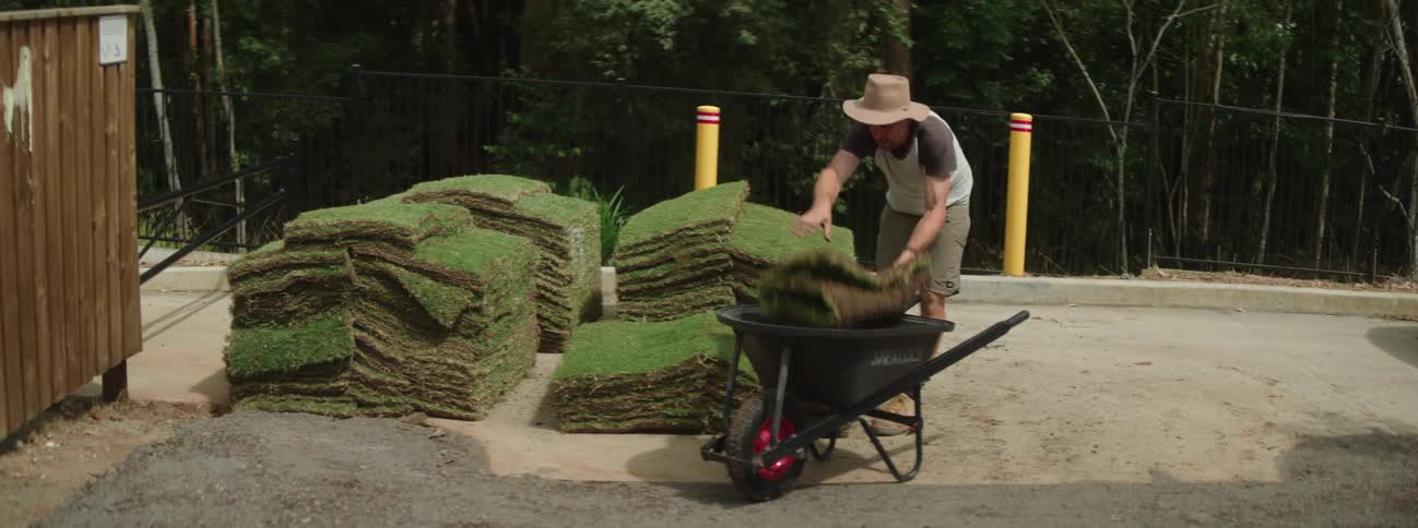 A man is stacking grass squares in the wheelbarrow