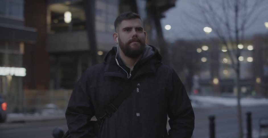 A man walking on a city sidewalk at night while wearing headphones