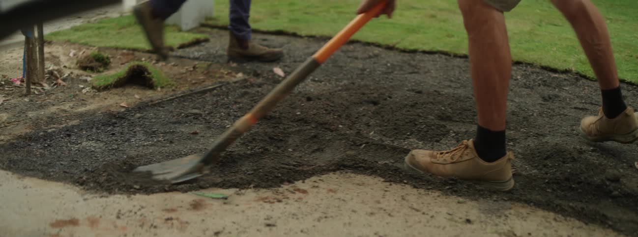 A man digging up dirt while laying sod on a lawn