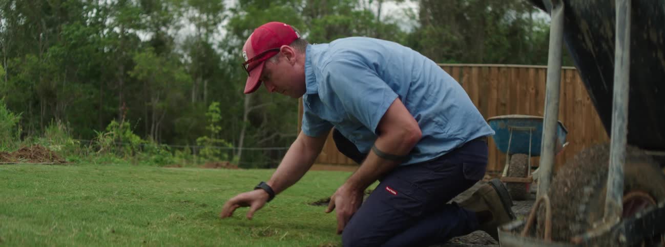 A man is outside kneeling as he lays down sod in his yard