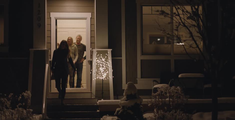 The front door of a house opens and a young woman hugs her mother as she walks out the door and down the steps